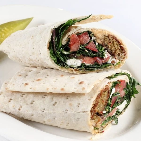 Two halves of a Persian wrap filled with falafel, greens, tomatoes, and feta cheese, with a pickle.
