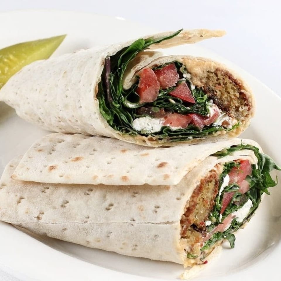 Two halves of a Persian wrap filled with falafel, greens, tomatoes, and feta cheese, with a pickle.