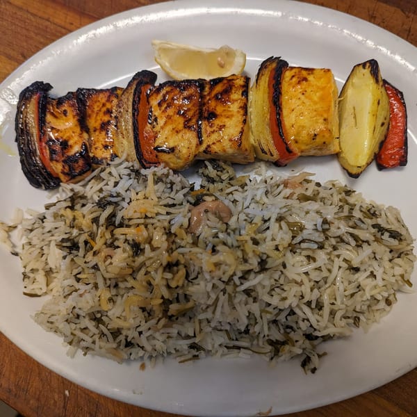 Grilled chicken and vegetable skewer with a lemon wedge, served alongside Persian herb rice.