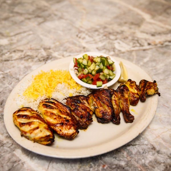 Grilled chicken kabobs with rice, a side salad, and a lemon wedge on a white plate.