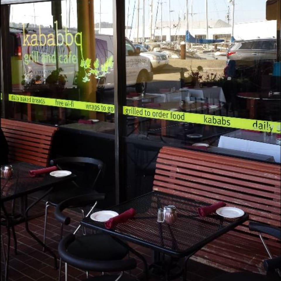 Outdoor seating area of Kababbq Grill & Café with tables, chairs, and a view of a marina.