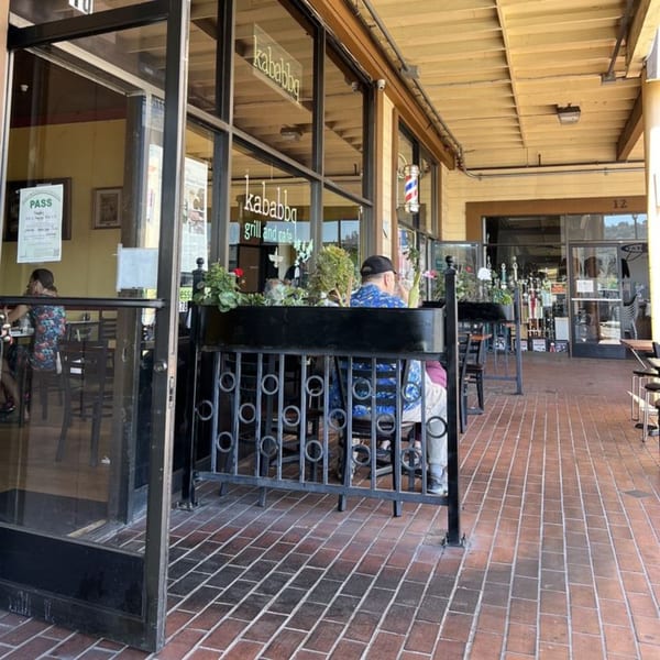 Outdoor patio seating at Kababbq Grill & Café with people dining and a brick walkway.