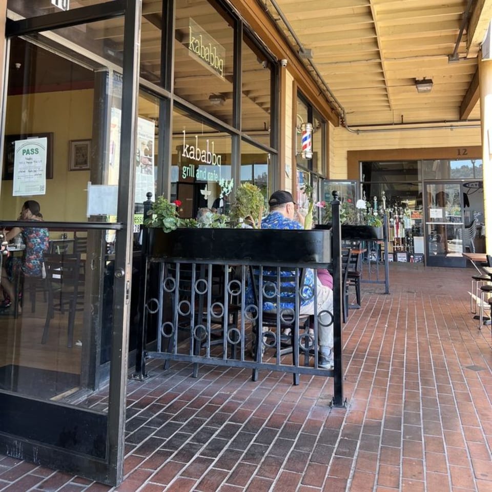 Outdoor patio seating at Kababbq Grill & Café with people dining and a brick walkway.