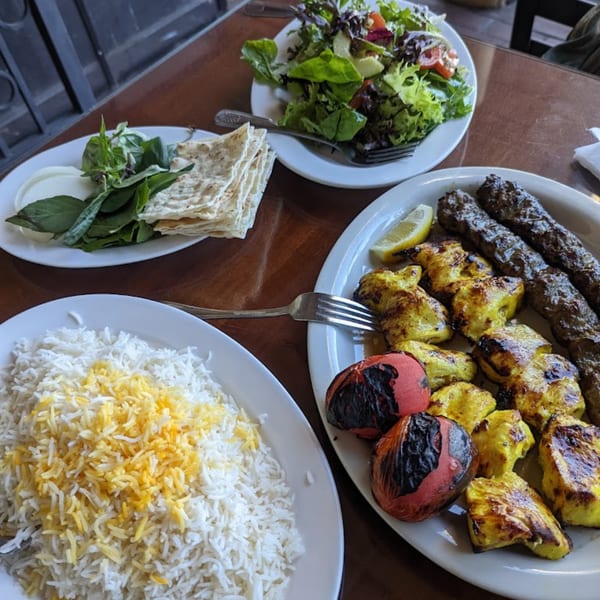 A Persian meal with rice, grilled chicken and beef kabobs, roasted tomatoes, salad, and flatbread.