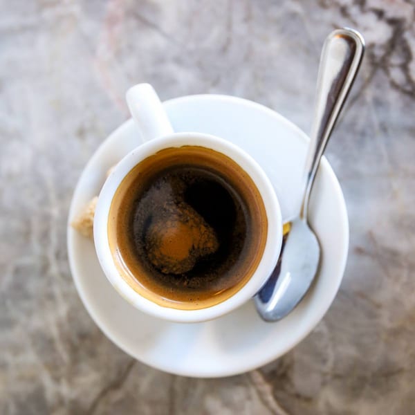 Overhead view of a white cup of dark coffee with a spoon on a marble table.
