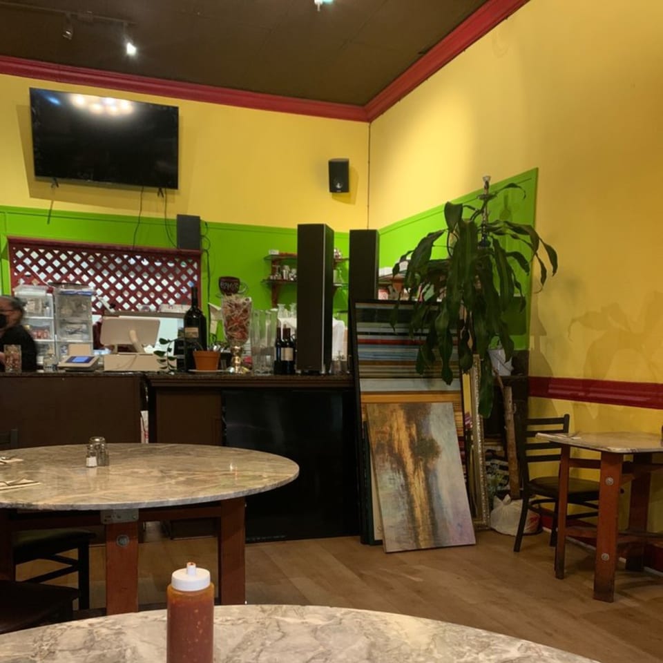 Interior of Kababbq Grill & Café with yellow and green walls, marble tables, and a counter area.