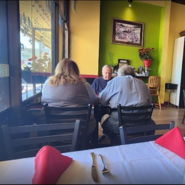 Three people seated at tables in a brightly lit restaurant with green and yellow walls.