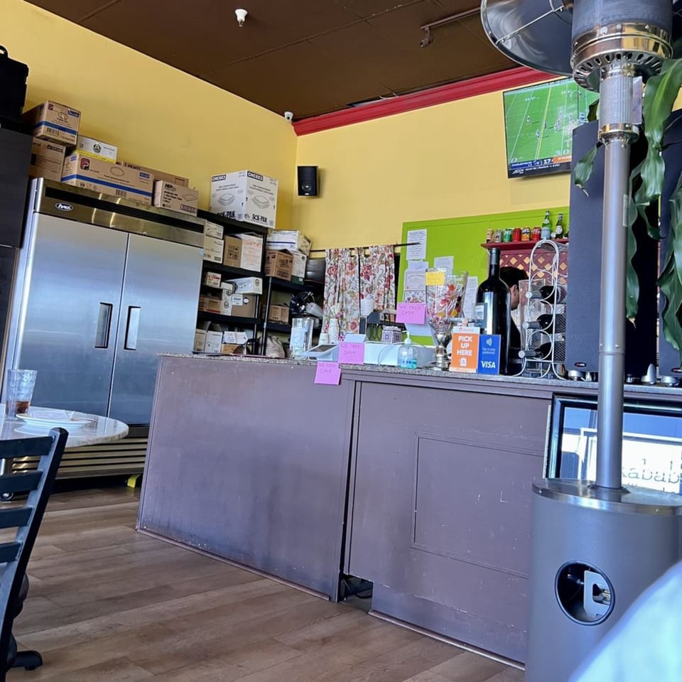 Interior view of Kababbq Grill & Café, showing the counter, refrigerators, and a TV playing sports.