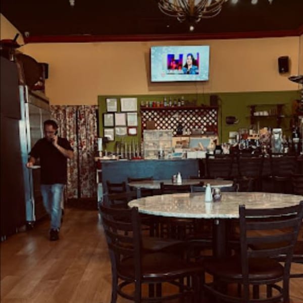 A man on the phone walks through the Kababbq Grill & Café dining room with empty tables.