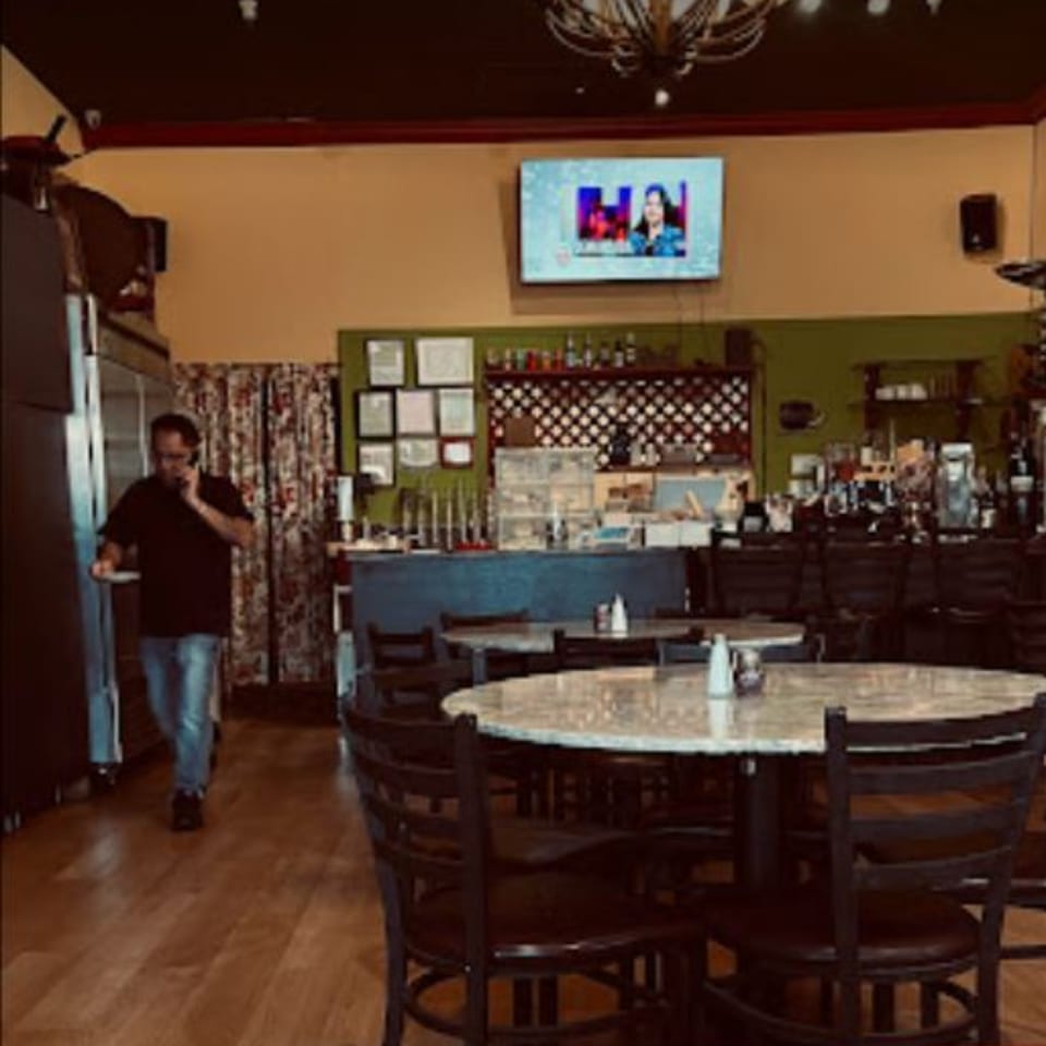 A man on the phone walks through the Kababbq Grill & Café dining room with empty tables.