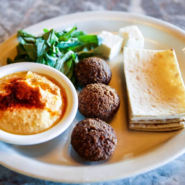 A plate of Persian appetizers with hummus, falafel, feta cheese, fresh herbs, and flatbread.