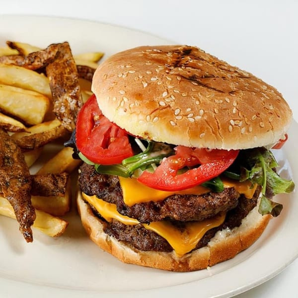 A double cheeseburger with lettuce, tomato, and a side of crispy fries on a white plate.